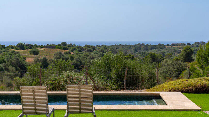 Infinity-Pool mit Holzliegen, Meerblick und üppiger Natur der Finca in Cales de Mallorca