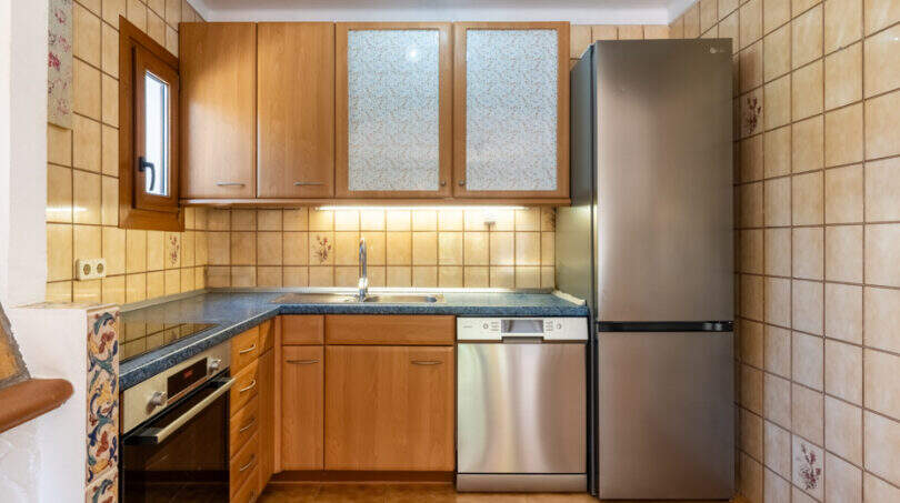 Küche mit Holzschränken, Edelstahlkühlschrank, Geschirrspüler und gefliesten Wänden im Apartment Cala Murada