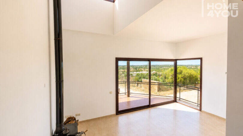 Helles Wohnzimmer mit Kaminofen, hoher Decke und großen Glasschiebetüren zur Terrasse mit Panoramablick, Ses Salines
