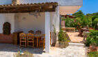 Überdachte Außenterrasse mit Holztisch und Stühlen, Steinboden und Gartenblick in Cala Murada