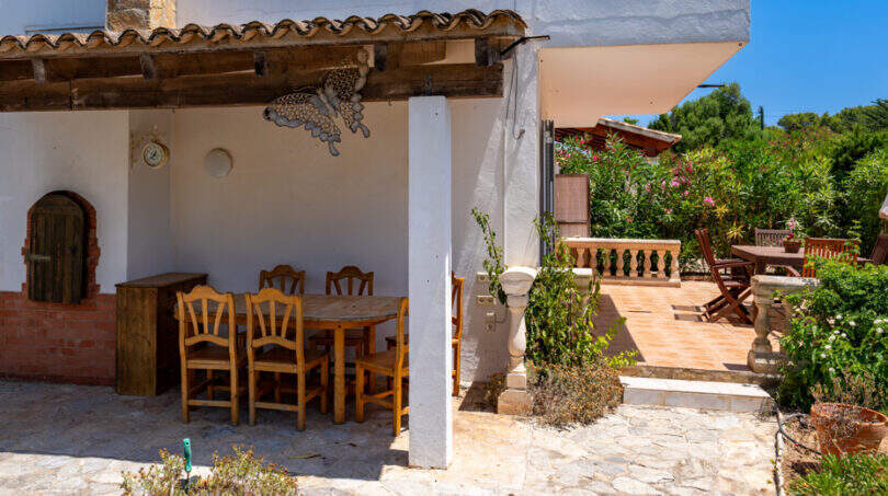Überdachte Außenterrasse mit Holztisch und Stühlen, Steinboden und Gartenblick in Cala Murada