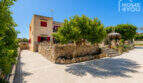 Außenansicht Finca in Cala Llombards mit Natursteinmauer, roter Fensterläden und mediterranem Baumbestand