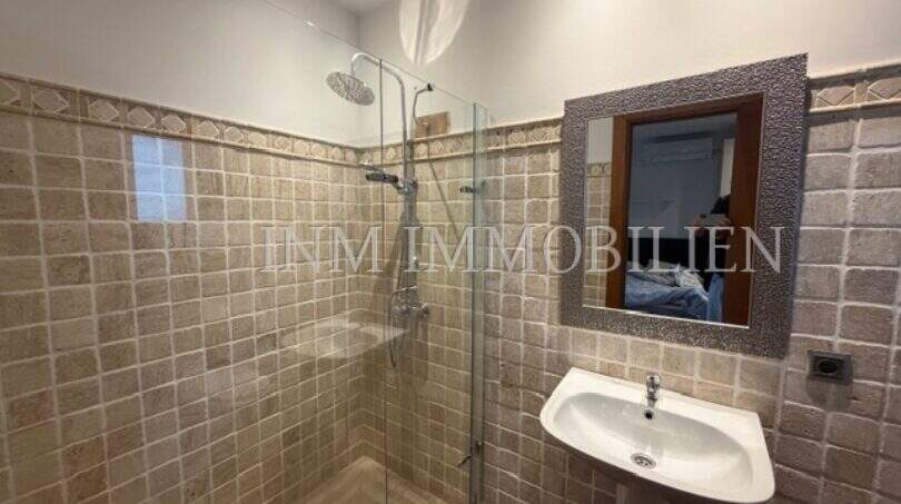 Badezimmer der Gästewohnung in Villa Marratxí mit Glasdusche, Natursteinwänden und elegantem Wandspiegel