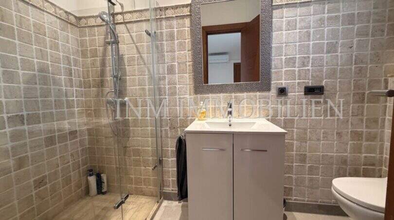 Baño moderno con ducha de cristal, mueble lavabo blanco y baldosas de piedra natural en las paredes en villa Marratxí