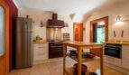 Amplia cocina de la villa de Cala Murada con isla de cocina, cocina de color burdeos, frigorífico de acero inoxidable y cuencos rústicos de terracota.