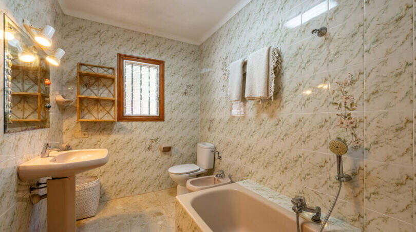 Cuarto de baño de la villa con azulejos de mármol, bañera, bidé, inodoro y toallero en Cala Murada