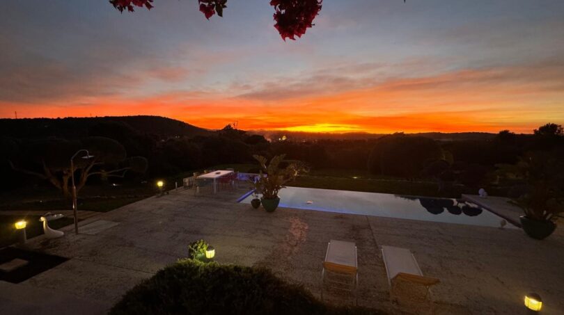Luxusfinca Son Carrió: beleuchteter Pool mit Bougainvillea und dramatischem Sonnenuntergang über der Landschaft