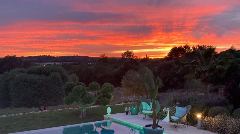 Luxusfinca Son Carrió: beleuchteter Pool bei dramatischem Sonnenuntergang mit Gartenanlage und Panoramablick