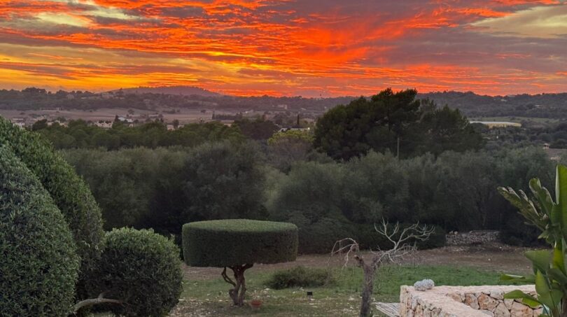 Luxusfinca Son Carrió: Gartenanlage mit spektakulärem Sonnenuntergang und weitem Panoramablick über die Landschaft.