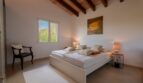 Helles Schlafzimmer der Luxusfinca in Son Carrió mit Holzbalkendecke, Doppelbett und Gartenblick