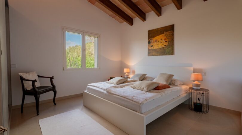 Helles Schlafzimmer der Luxusfinca in Son Carrió mit Holzbalkendecke, Doppelbett und Gartenblick