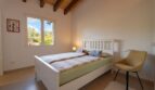 Helles Schlafzimmer der Luxusfinca in Son Carrió mit Holzbalkendecke, Doppelbett und Gartenblick