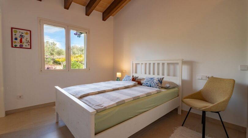 Helles Schlafzimmer der Luxusfinca in Son Carrió mit Holzbalkendecke, Doppelbett und Gartenblick