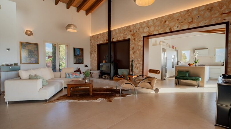 Lichtdurchflutetes Wohnzimmer der Luxusfinca in Son Carrió mit Natursteinwand, Kamin und offenem Küchenbereich