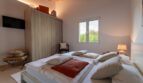 Helles Schlafzimmer der Luxusfinca in Son Carrió mit Doppelbett, Holzbalkendecke und Naturblick durchs Fenster.