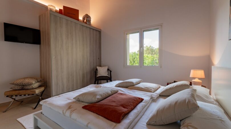 Helles Schlafzimmer der Luxusfinca in Son Carrió mit Doppelbett, Holzbalkendecke und Naturblick durchs Fenster.