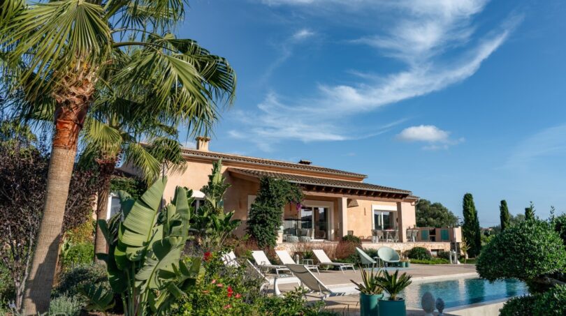 Luxusfinca Son Carrió: mediterrane Villa mit Pool, Liegestühlen, Palmen und tropischem Garten unter blauem Himmel.