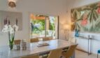 Elegantes Esszimmer der Luxusfinca in Son Carrió mit Holztisch, Naturblick durch Glasschiebetür und tropischer Wanddekoration.