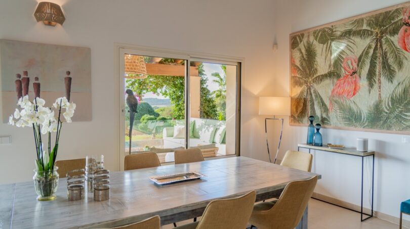Elegantes Esszimmer der Luxusfinca in Son Carrió mit Holztisch, Naturblick durch Glasschiebetür und tropischer Wanddekoration.