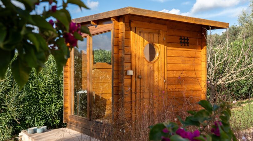 Außensauna aus Holz mit Glasfront und Bullauge im Garten der Luxusfinca in Son Carrió