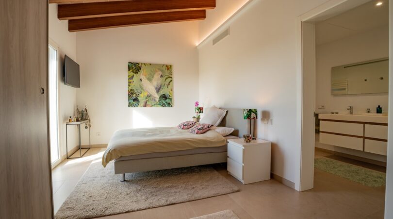 Helles Schlafzimmer der Luxusfinca in Son Carrió mit Holzbalkendecke, Doppelbett und angrenzendem Badezimmer