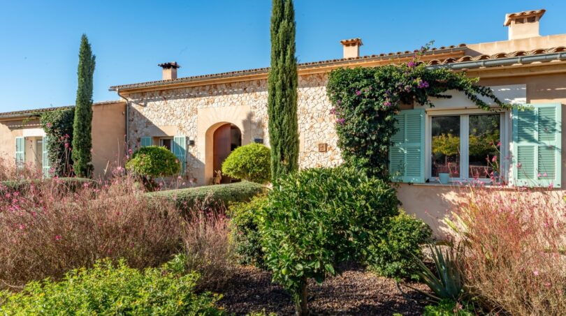 Außenansicht Luxusfinca Son Carrió mit Natursteinmauern, grünen Fensterläden und mediterranem Garten