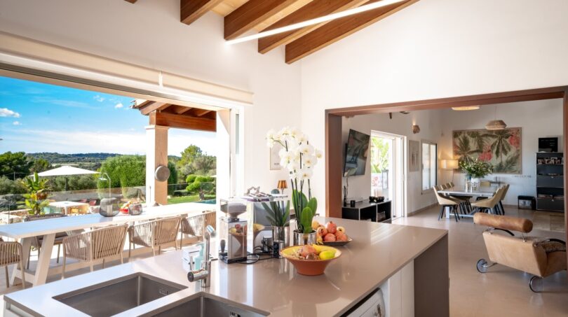 Offene Luxusküche mit Kochinsel, Holzbalkendecke und Panoramablick auf die mallorquinische Landschaft