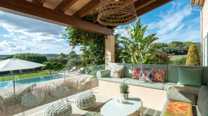 Überdachte Terrasse mit mint-grüner Lounge, Pool und Gartenblick der Luxusfinca in Son Carrió