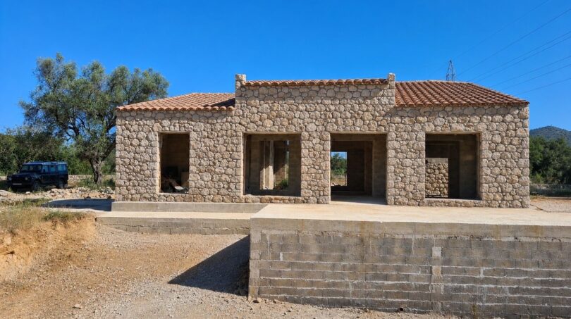Rohbau einer Naturstein-Finca in Artà mit Terrakotta-Ziegeldach und mediterraner Architektur unter blauem Himmel.