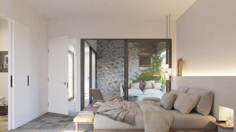 Helles Schlafzimmer mit Doppelbett, Natursteinboden und Glasschiebetür zum mediterranen Innenhof der Finca in Artà.