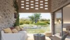 Überdachte Terrasse mit Natursteinwänden, weißem Sofa und Blick auf mediterranen Garten, Finca Artà