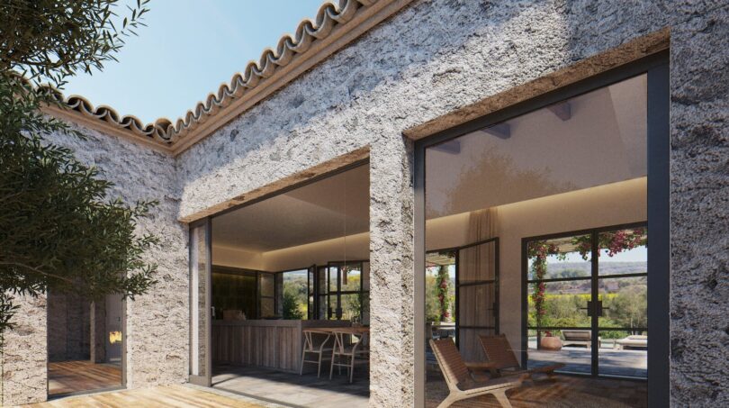 Holzterrasse einer Neubau-Finca in Artà mit Natursteinwänden, Terrakotta-Dach und großen Glasfronten zum Innenbereich