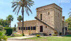Außenansicht exklusive Finca in Colònia de Sant Jordi: Historisches Steingebäude mit Turm, Palmen und gepflegtem Garten.