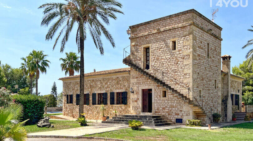 Außenansicht exklusive Finca in Colònia de Sant Jordi: Historisches Steingebäude mit Turm, Palmen und gepflegtem Garten.