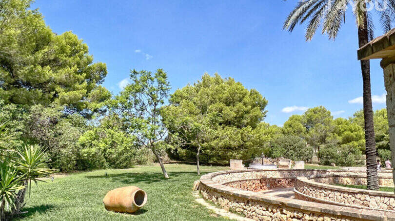 Weitläufiger Garten der Finca mit Palme, Steinmauer, Amphitheater-Terrasse und dekorativem Tonkrug