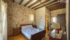 Rustikales Schlafzimmer mit Steinwand, Holzbalkendecke, Doppelbett und Parkettboden der Finca