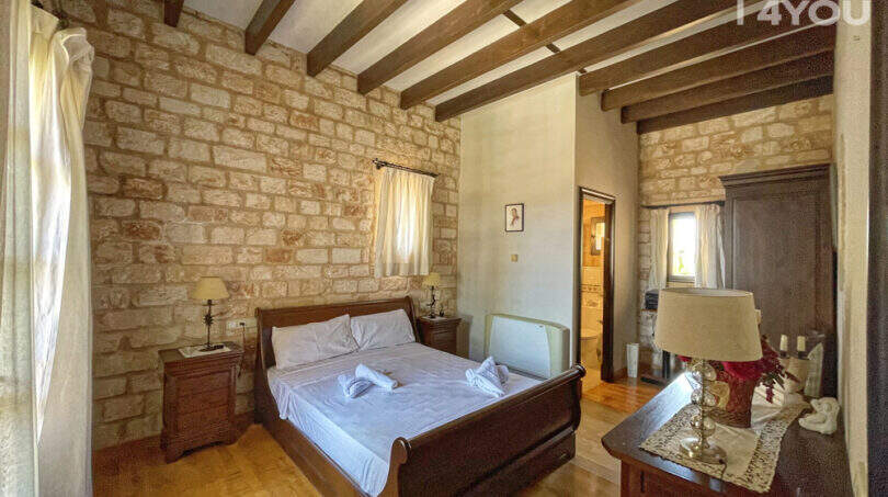 Rustikales Schlafzimmer mit Steinwand, Holzbalkendecke, Doppelbett und Parkettboden der Finca