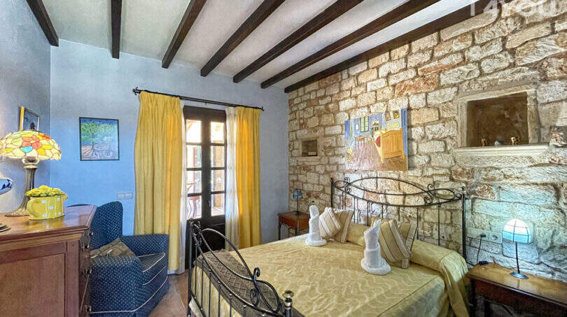 Rustikales Schlafzimmer der Finca mit Natursteinwand, Holzbalkendecke, Doppelbett und gelbem Dekor.