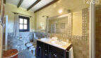 Elegantes Badezimmer der Finca mit Doppelwaschbecken, Natursteinwand, Holzbalkendecke und Dusche.