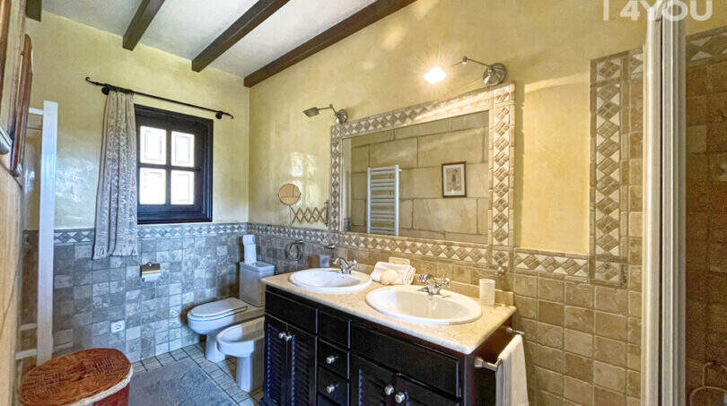 Elegantes Badezimmer der Finca mit Doppelwaschbecken, Natursteinwand, Holzbalkendecke und Dusche.