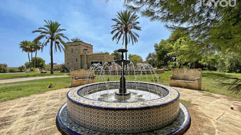Gartenanlage der Finca mit kunstvollem Mosaikbrunnen, Palmen und historischem Gutshaus in Colònia de Sant Jordi.