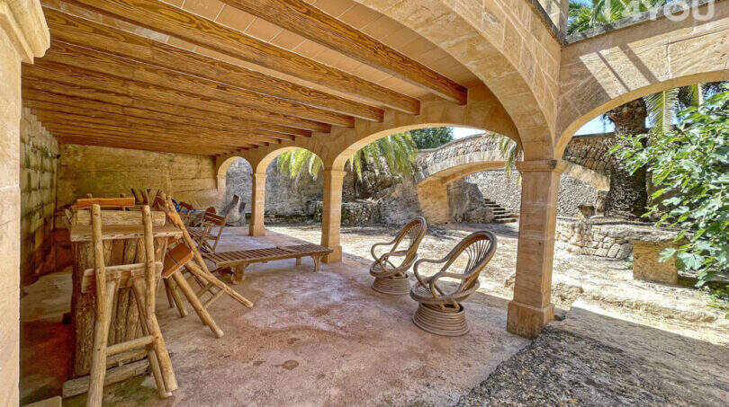 Überdachte Terrasse mit Steinbögen, Holzbalkendecke und Rattanmöbeln der exklusiven Finca in Colònia de Sant Jordi