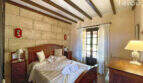 Schlafzimmer der Finca mit Holzbalkendecke, Steinwand, Doppelbett und Holzmöbeln in Colònia de Sant Jordi