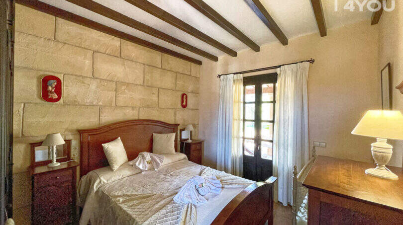 Schlafzimmer der Finca mit Holzbalkendecke, Steinwand, Doppelbett und Holzmöbeln in Colònia de Sant Jordi