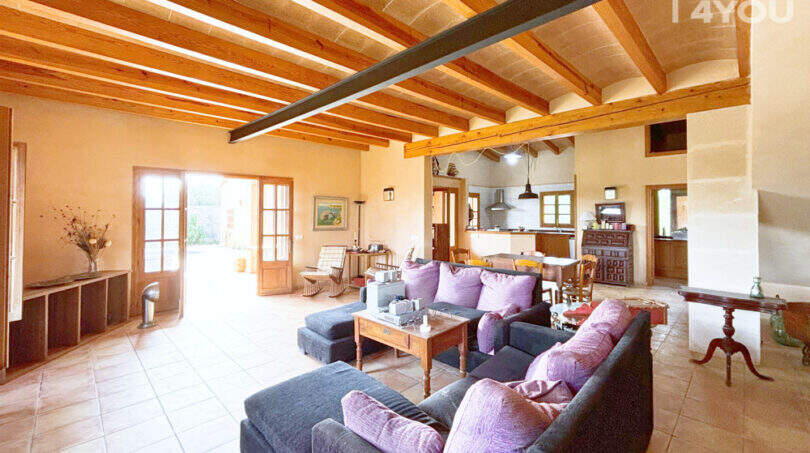 Geräumiges Wohnzimmer der Finca in Ses Salines mit Holzbalkendecke, Sofagruppe und offenem Küchenbereich
