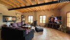 Wohnzimmer der Finca in Ses Salines mit Holzbalkendecke, dunklem Sofa, Kaminofen und großem TV.