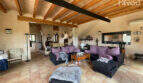 Geräumiges Wohnzimmer der Finca in Ses Salines mit Holzbalkendecke, dunklen Sofas und Terrakottafliesen.