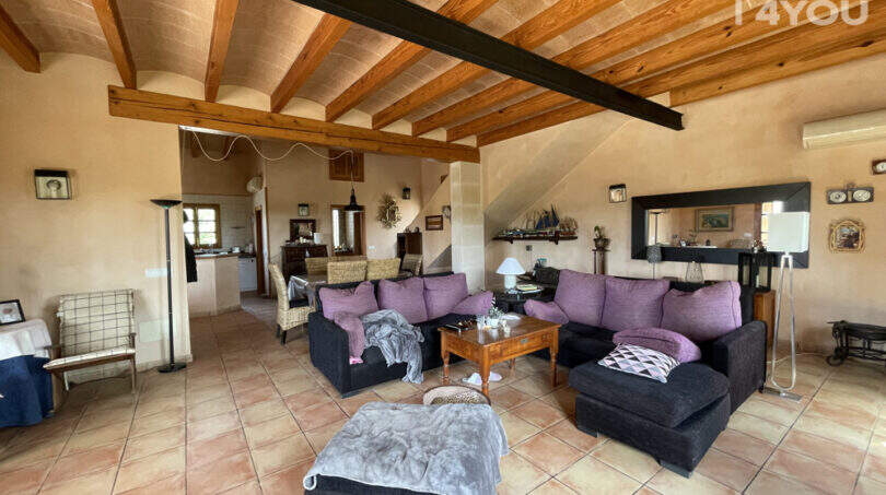 Geräumiges Wohnzimmer der Finca in Ses Salines mit Holzbalkendecke, dunklen Sofas und Terrakottafliesen.