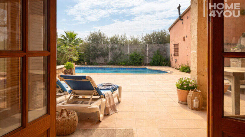 Blick durch Holztüren auf sonnige Terrasse mit Liegestühlen und Pool der Finca in Ses Salines