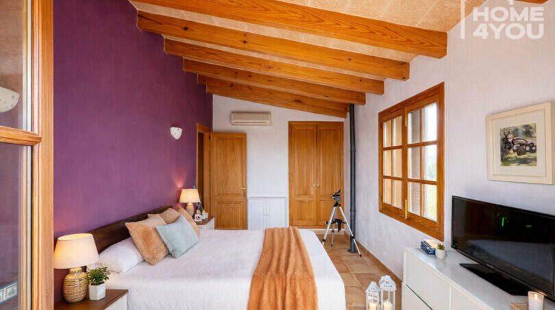 Schlafzimmer der Finca Ses Salines mit Holzbalkendecke, lila Akzentwand und mediterranem Charme.